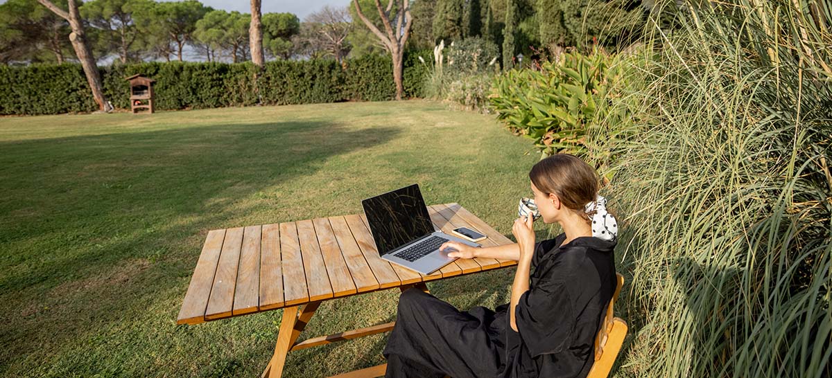 woman outside drinking coffee and using a laptop